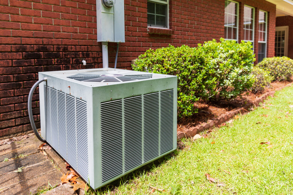 air conditioner system next to home, brick and bushes with clean yard.