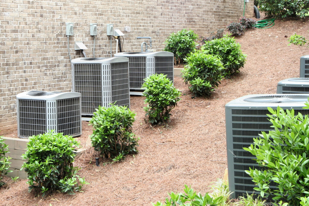 Multiple residential air conditioning units in a landscaped area of a home.